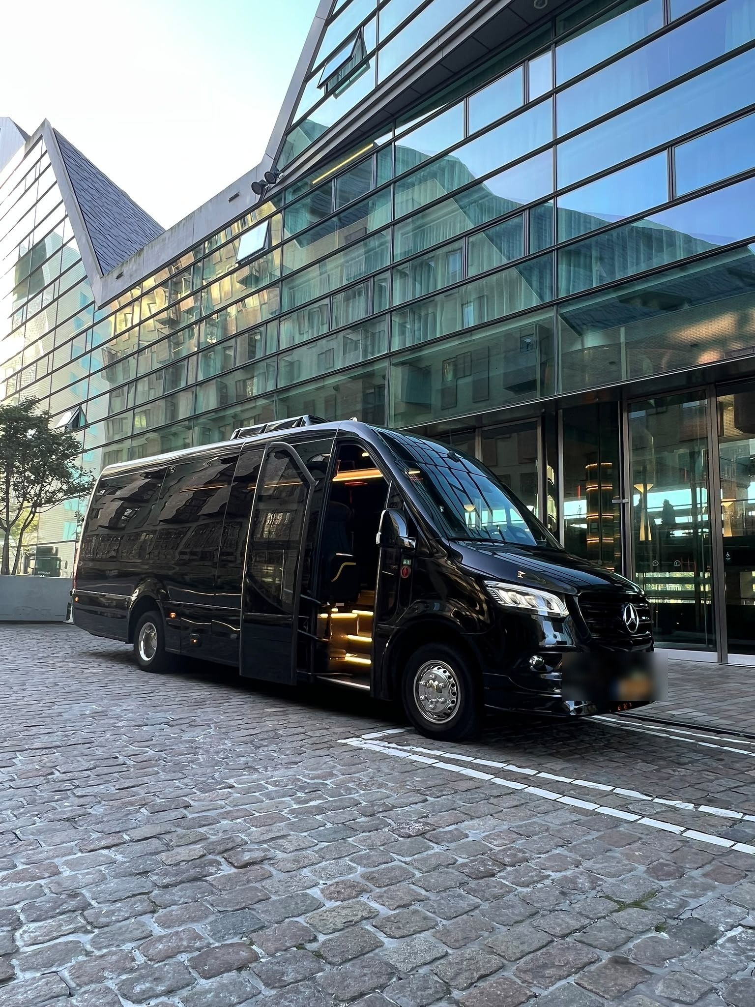 Premium transporter — black Mercedes-Benz Sprinter outside a glass hotel